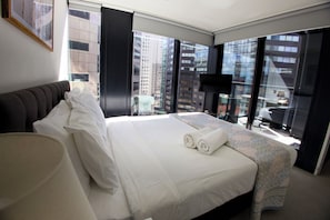 A hotel room with a large bed, a view of the cityscape through floor-to-ceiling windows, a flat-screen TV, and a modern design. - Luxury City Retreat with Balcony Pool and Gym (Auckland)