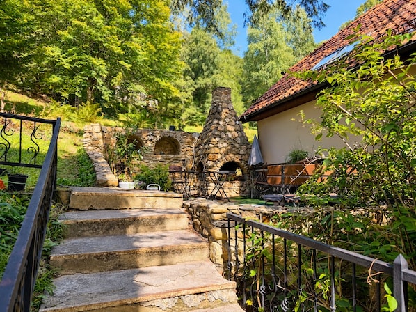 A stone staircase leading to a rustic outdoor area with a stone oven and seating.