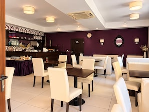 A restaurant with a purple wall, white chairs, and a bar area with shelves. - Renessans Rehabilitation Center (Pokrzywna)