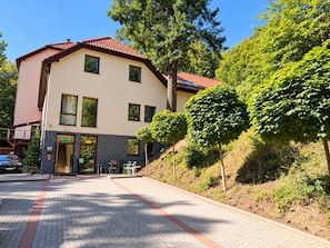 A two-story building with a red-tiled roof, a paved entrance, and a small outdoor seating area.