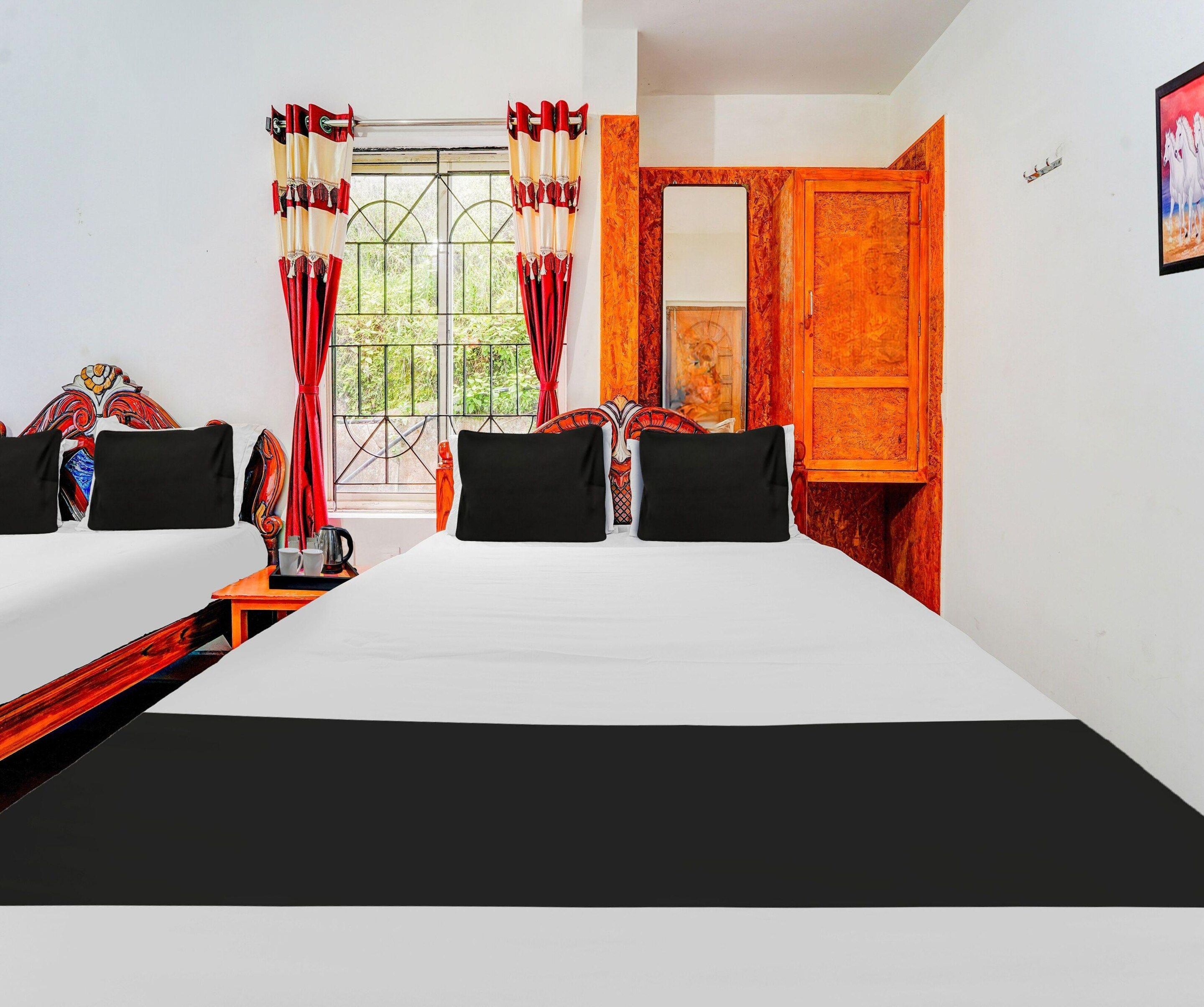Habitación de hotel con una cama grande, dos mesitas de noche, una ventana con cortinas, una puerta y una pequeña mesa con una tetera y tazas.