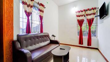 A furnished room with a leather sofa, a small table, and two windows with red curtains.