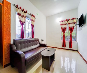 Une chambre meublée avec un canapé en cuir, une petite table et deux fenêtres ornées de rideaux rouges.
