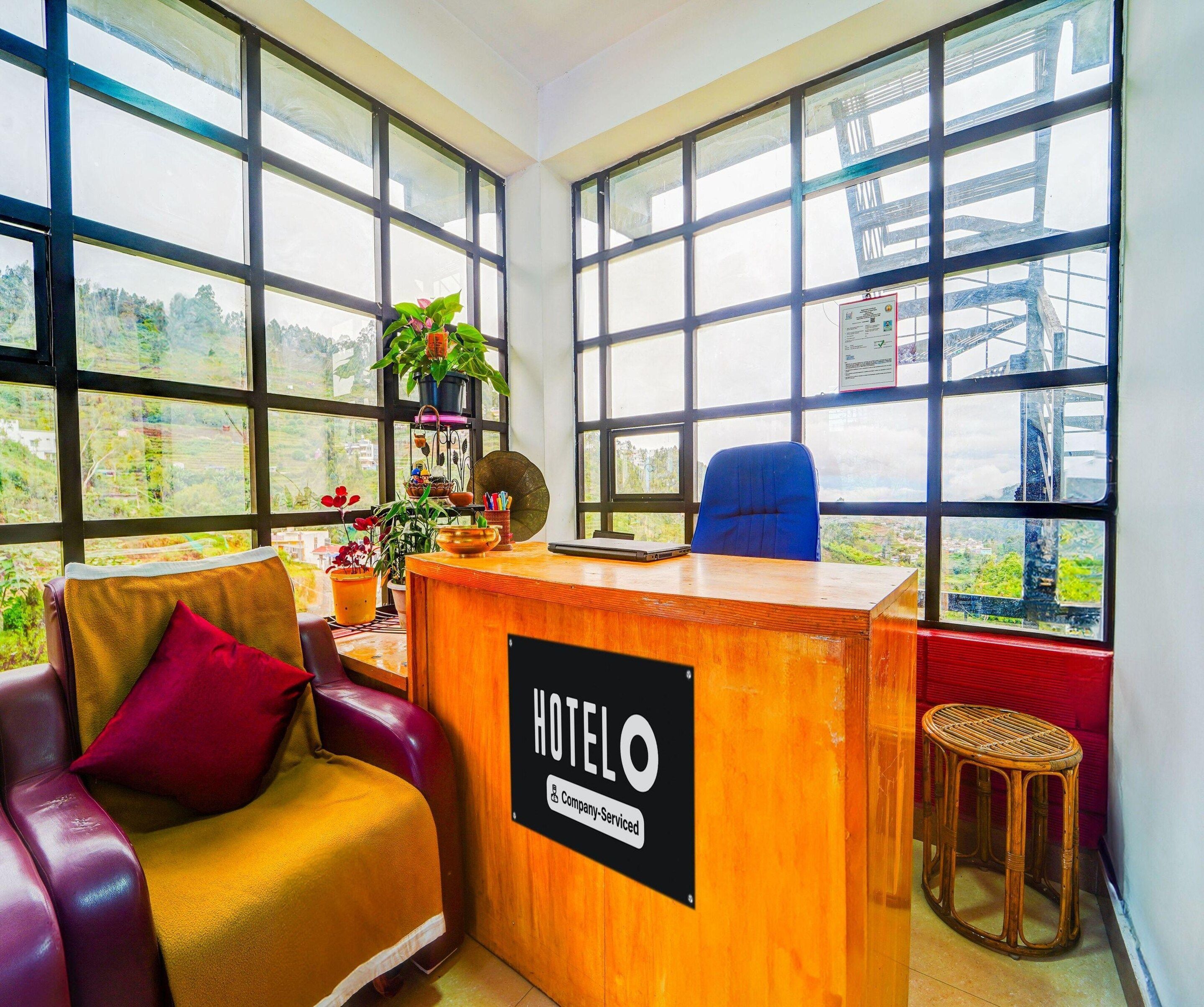 Un mostrador de recepción de hotel con un letrero que indica servicio de empresa. Se observan grandes ventanales con vistas a zonas verdes y un puente.