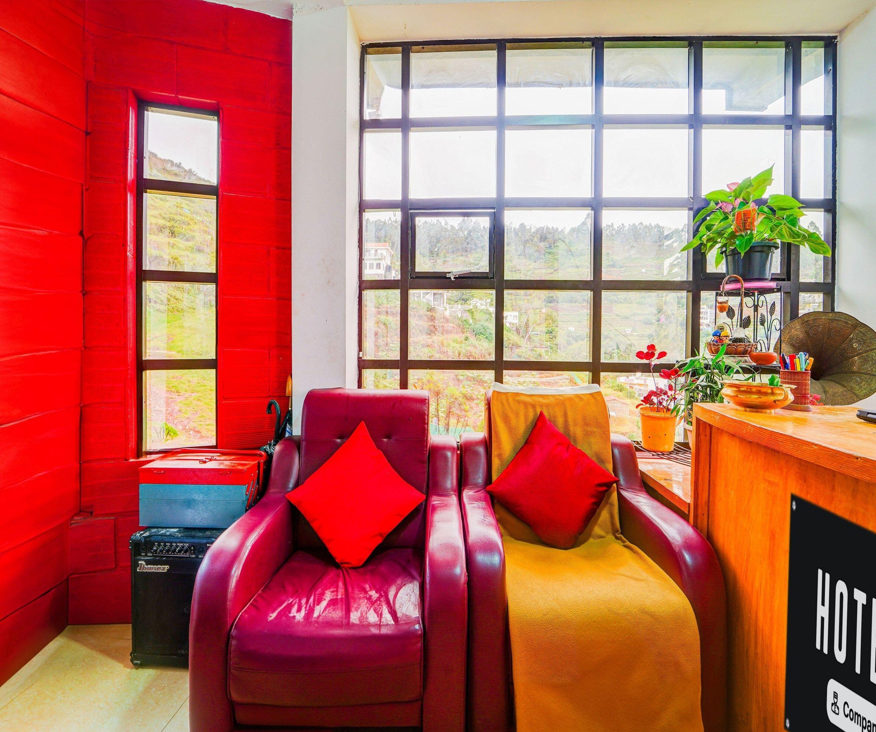 Une chambre d’hôtel avec un mur rouge, une grande fenêtre, un fauteuil en cuir, un bureau en bois et une enseigne sur laquelle on peut lire « HÔTEL ».