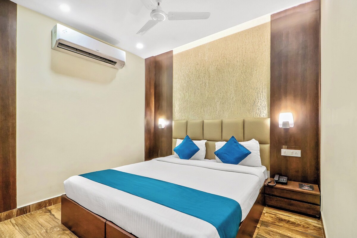 Ein Hotelzimmer mit einem Bett, einem Deckenventilator, einer Klimaanlage, einem Nachttisch mit Telefon und einer Wandleuchte.