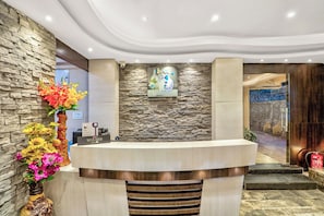 Zona de recepción con pared de piedra, mostrador de recepción y un elemento decorativo en la pared.