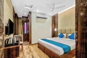 Ein Hotelzimmer mit einem Bett, einem Schreibtisch mit Stuhl, einem Fernseher, einer Klimaanlage und einem Deckenventilator.