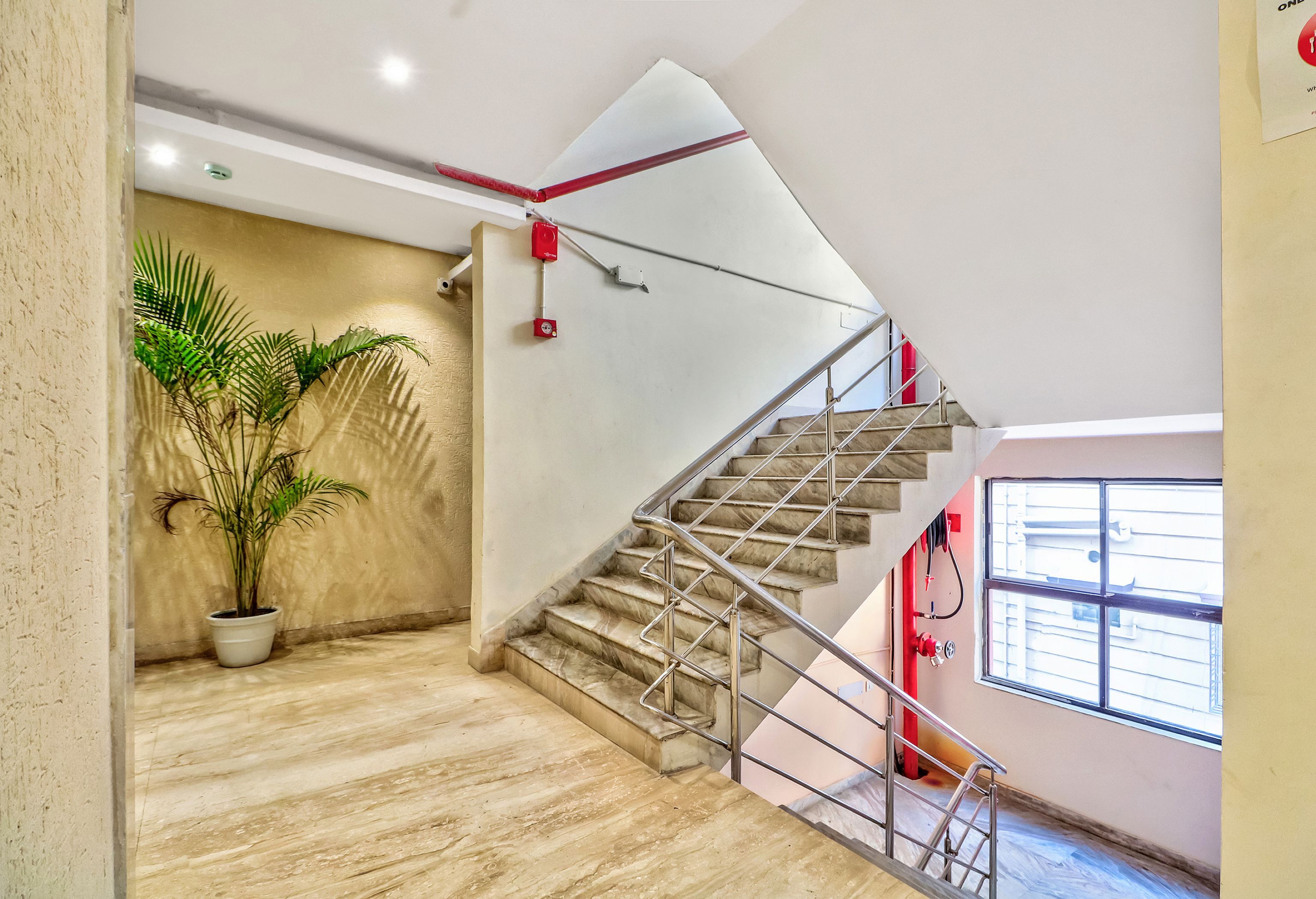 Una escalera con barandilla de metal, una planta en maceta y un detector de incendios rojo en la pared.
