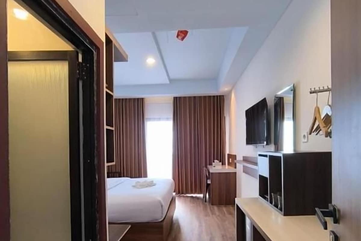 A hotel room with a bed, a desk, a television, and a wardrobe.