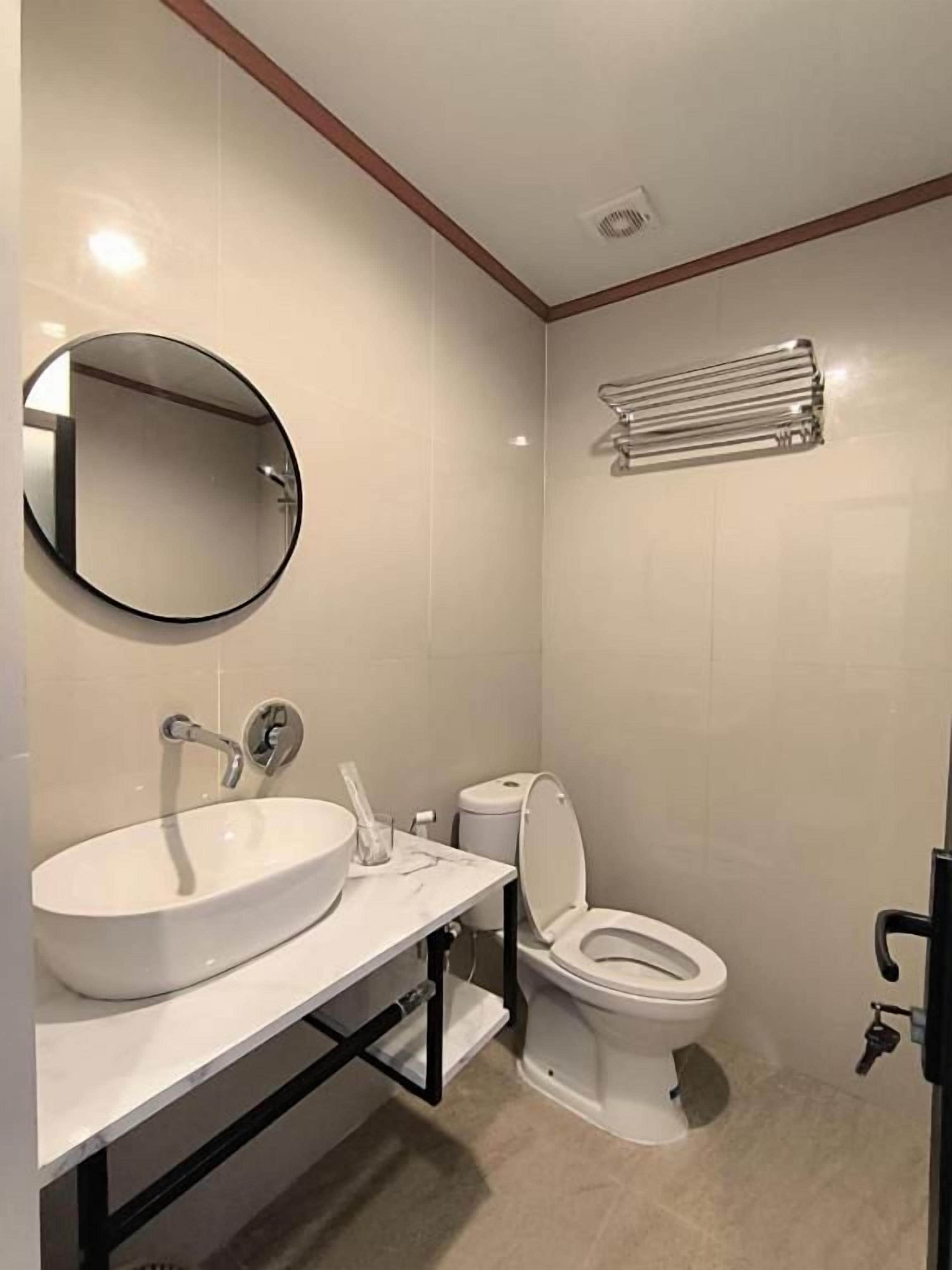 A bathroom with a white sink, toilet, and a round mirror.