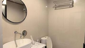 A bathroom with a white sink, toilet, and a round mirror.