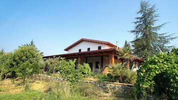 Una casa de dos pisos con techo rojo, rodeada de follaje y árboles.