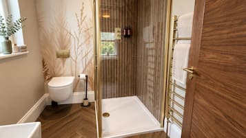 A bathroom with a white toilet, a shower enclosure, and a wooden floor.