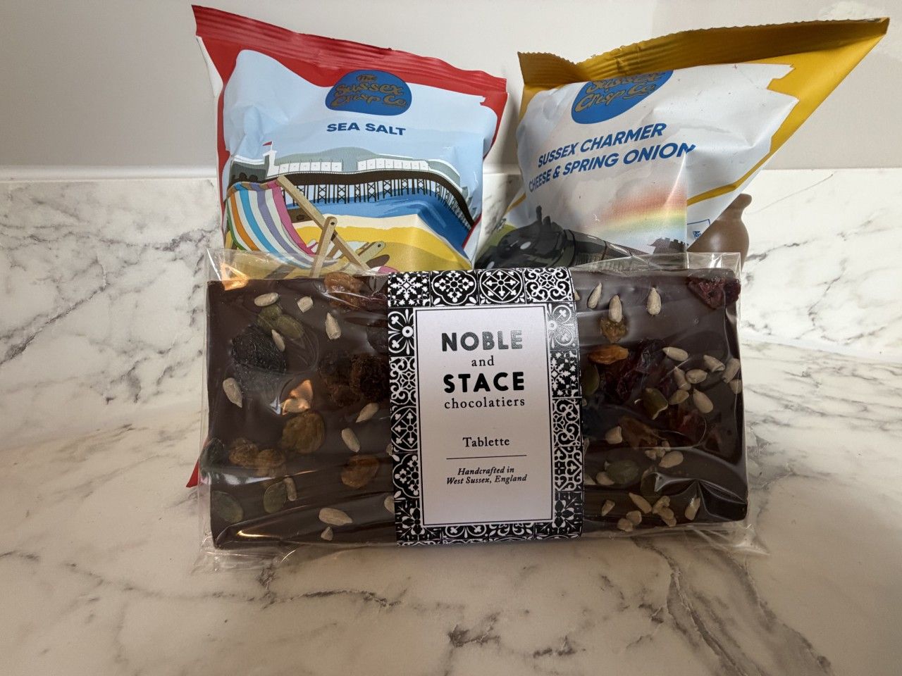 A gift basket with a label reading 'Noble and Stace chocolatiers Tablette' and includes items like sea salt and Sussex chameleon cheese & spring onion.