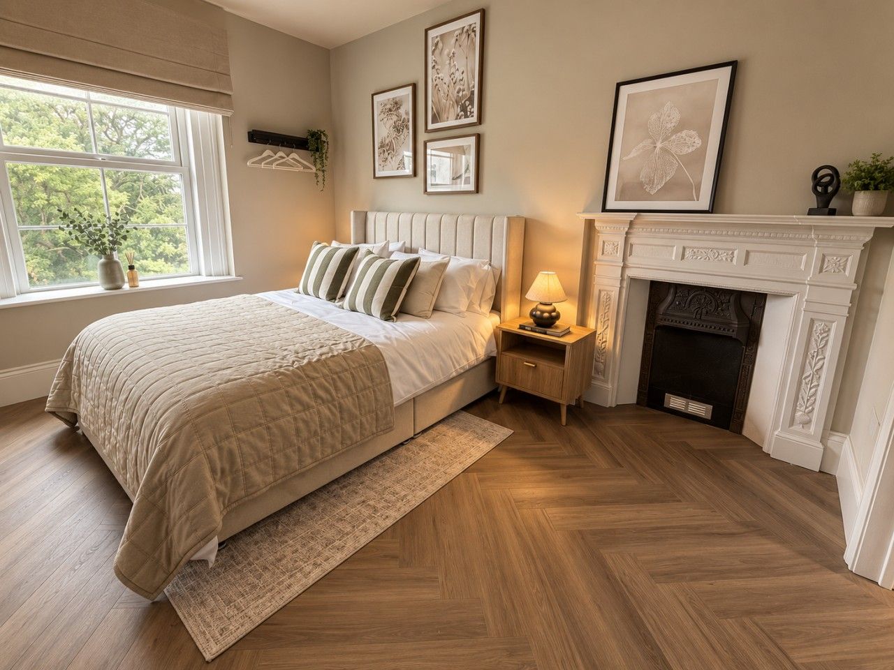 A bedroom with a bed, bedside table, lamp, fireplace, and framed pictures on the wall.