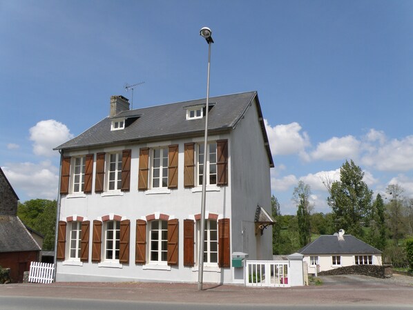 A two-story building with a white facade and brown shutters, a chimney, and a small attached structure with a white fence.