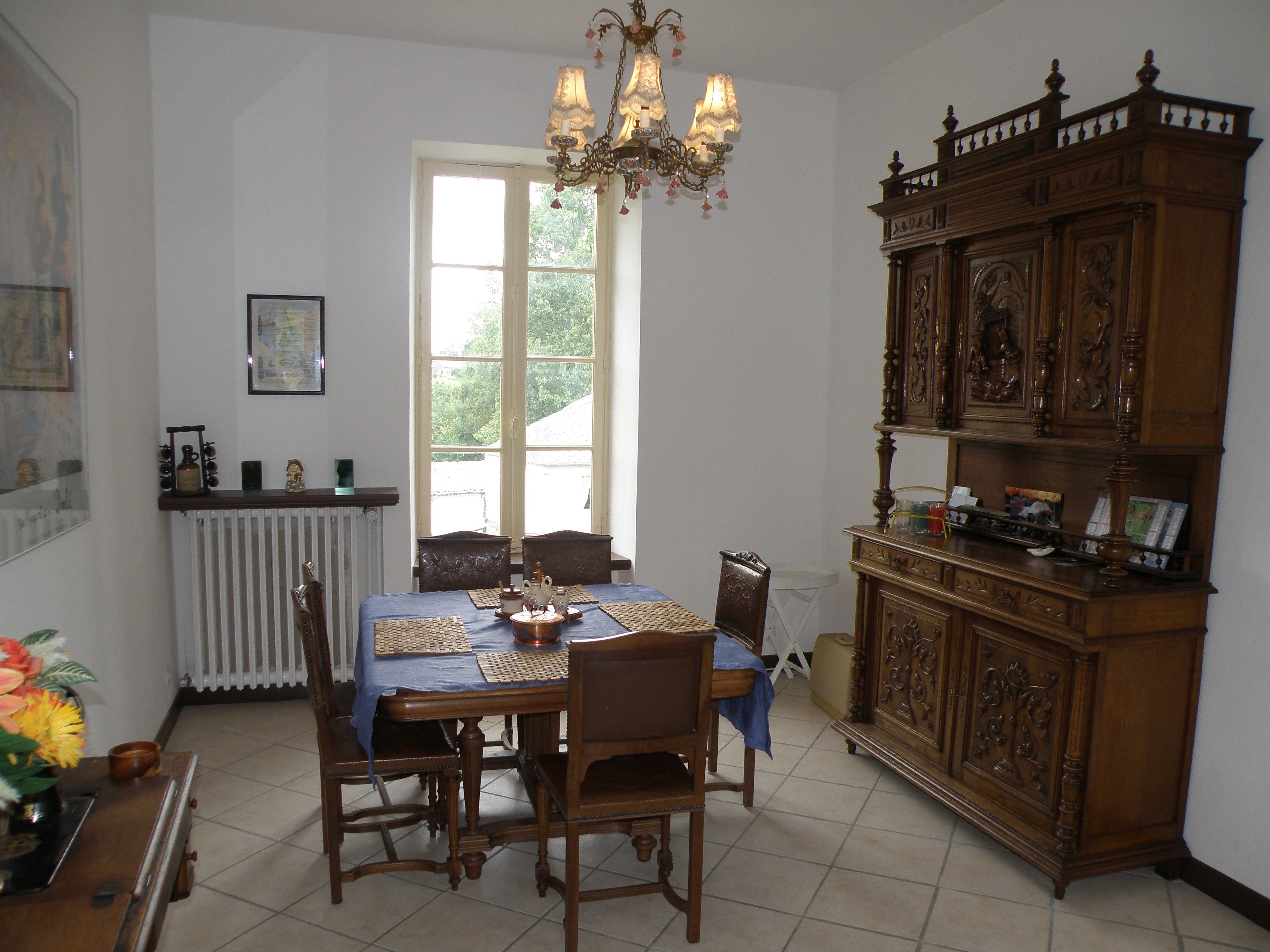 Une salle à manger avec une table dressée pour quatre personnes, un lustre et un buffet en bois orné de sculptures complexes.