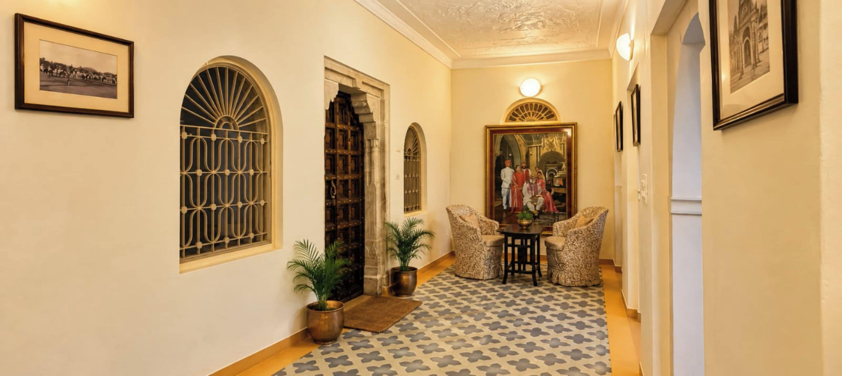 A hallway with arched windows, a framed painting, and patterned flooring.