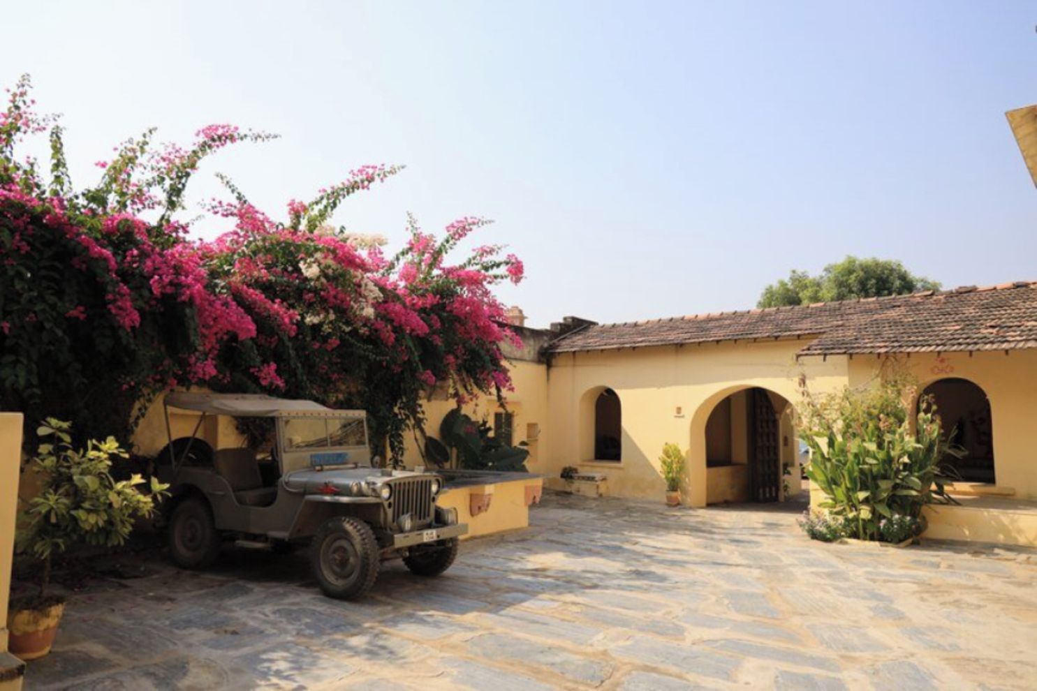 A courtyard with a vintage car, a building with arches, and flowering plants.