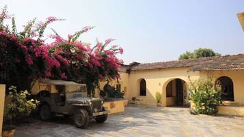 A courtyard with a vintage car, a building with arches, and flowering plants.