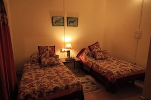 A small, cozy room with two single beds, a nightstand with a lamp, and two framed pictures on the wall.