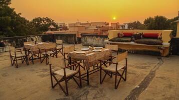 A rooftop terrace with tables and chairs, a sofa, and a view of the sunset.
