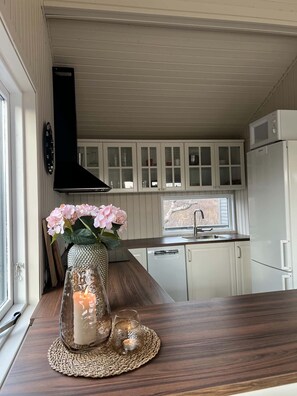 A kitchen with white cabinets, a black range hood, a microwave, and a refrigerator.
