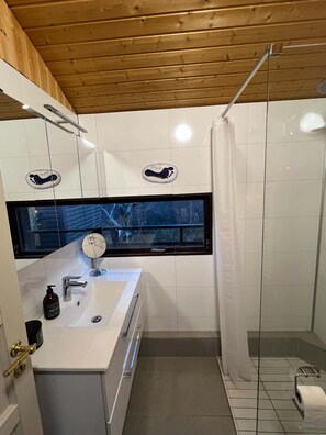 Un bany modern amb sostre de fusta, una finestra gran, un lavabo amb mirall i una zona de dutxa.