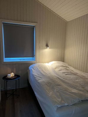A bedroom with a bed, a window, a wall-mounted light, and a small table with dice.