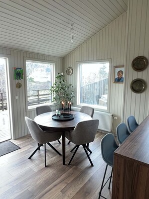 A dining area with a round table, six chairs, a potted plant, and a view of the outside through large windows.