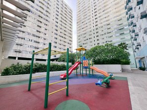 Un parc infantil amb tobogans i elements per escalar, envoltat d'edificis residencials alts.