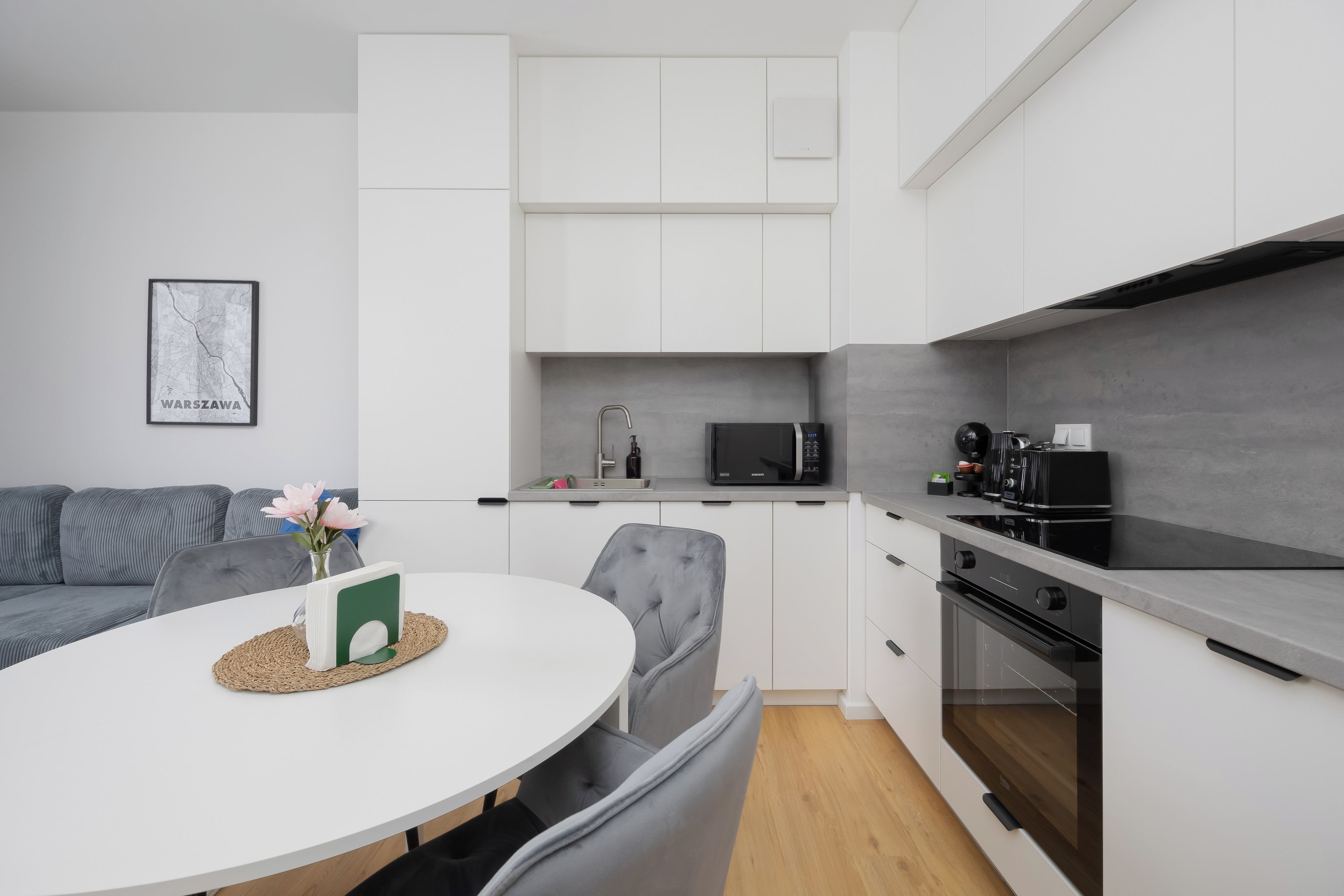 Una cocina moderna con armarios blancos, microondas, cafetera y un comedor con mesa redonda y sillas grises tapizadas.