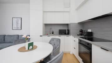 A modern kitchen with white cabinetry, a microwave, a coffee machine, and a dining area with a round table and grey upholstered chairs.