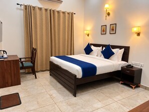 A hotel room with a bed, bedside table, chair, and a desk with a kettle. - VITS Select Kailasha Garden Ayodhya (Faizabad)
