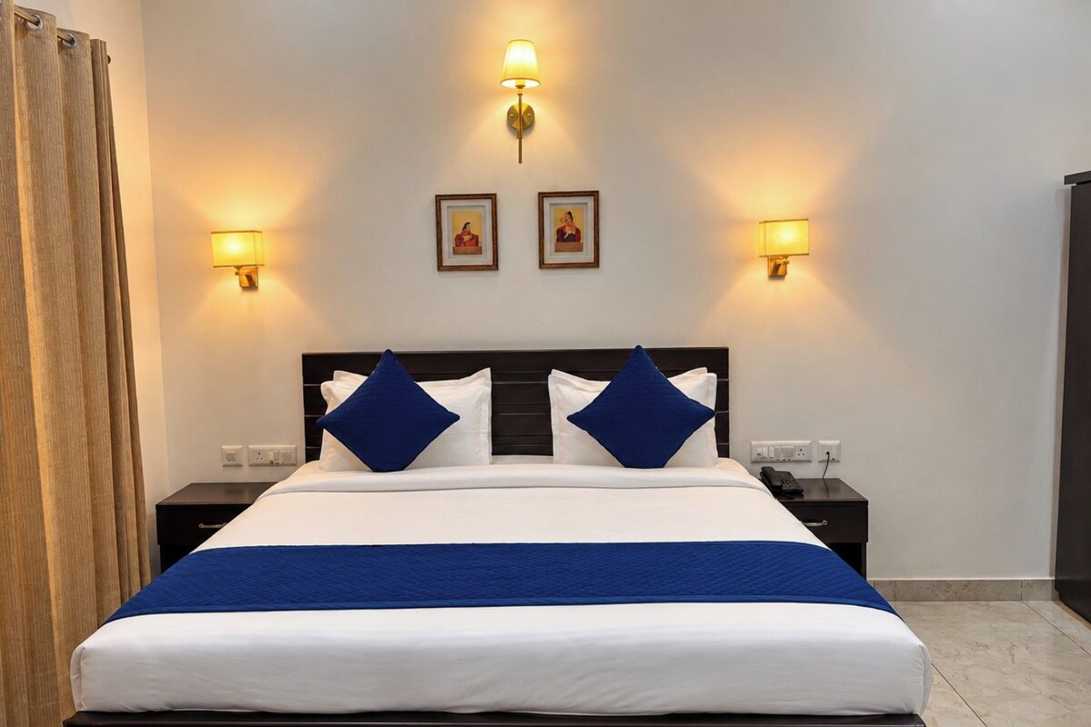 A hotel room with a bed, two bedside tables, a nightstand, a lamp, and a curtain.