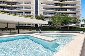 Een modern hotel met een zwembad, terras en een meerlaags gebouw met balkons.