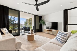 A modern living room with a flat-screen TV, a ceiling fan, and a large sliding glass door leading to an outdoor area.