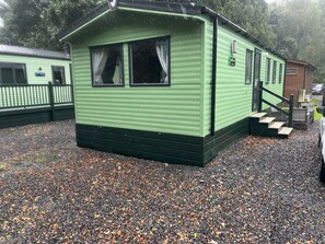 A green mobile home with a small porch and a set of stairs leading to the entrance. - Harmony | Cosy 3BR Retreat in Windermere | Pet Friendly (Middleton)