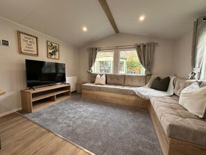 A living room with a television, sofa, and a window with curtains. - Harmony | Cosy 3BR Retreat in Windermere | Pet Friendly (Middleton)