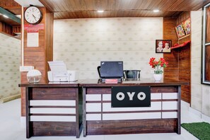 A reception desk with a clock, a Lenovo laptop, a printer, and a vase with flowers. - Hotel O Amma Bhau Residency (Mumbai)