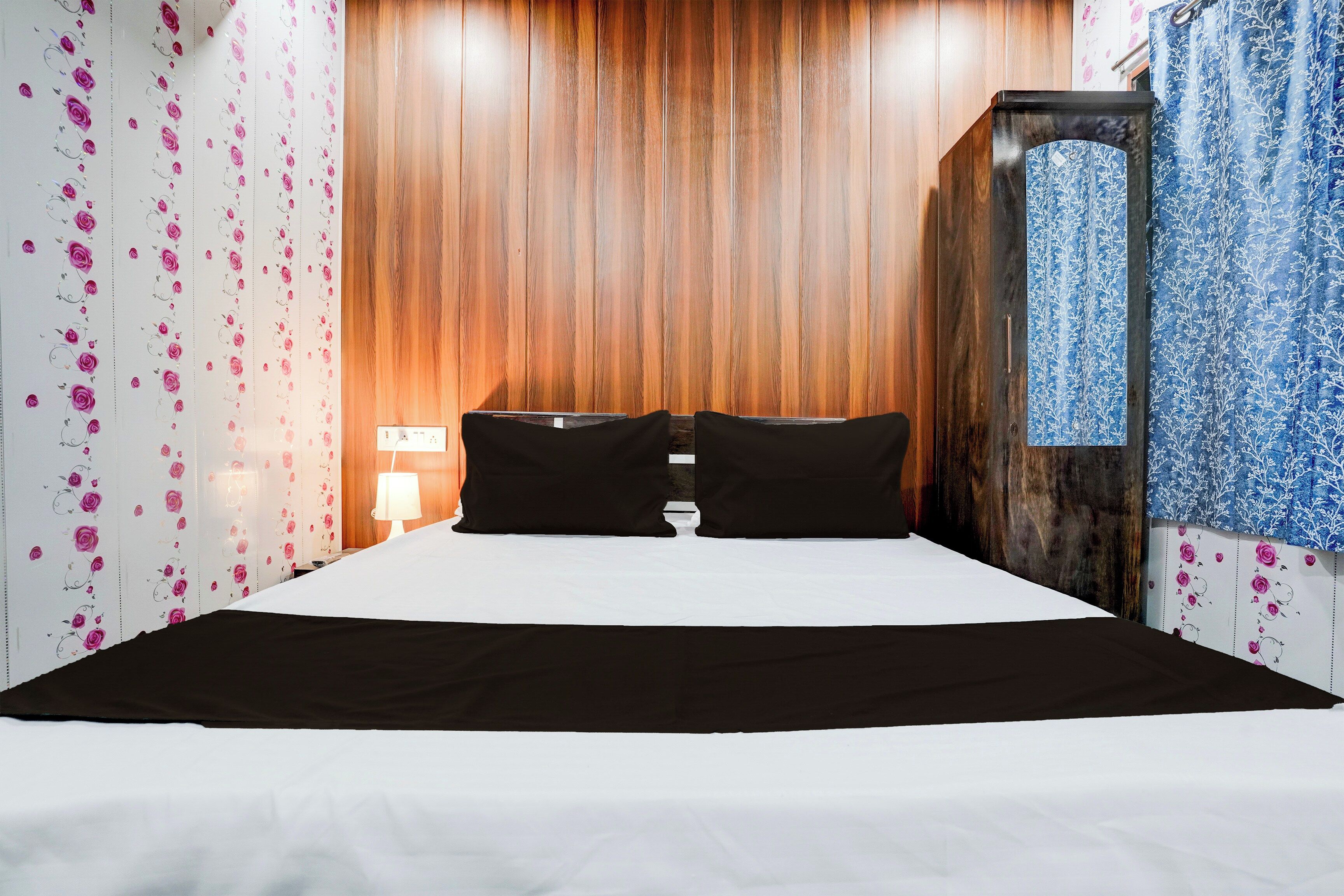 Una habitación de hotel con cabecera de madera, una cama con ropa de cama blanco y negro y papel tapiz floral.