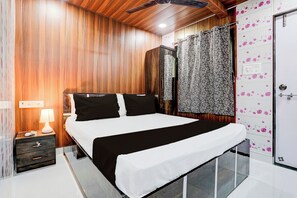 A modern bedroom with a wooden wall, a bed with black and white bedding, a nightstand with a lamp, and a door with floral wallpaper. - Hotel O Amma Bhau Residency (Mumbai)