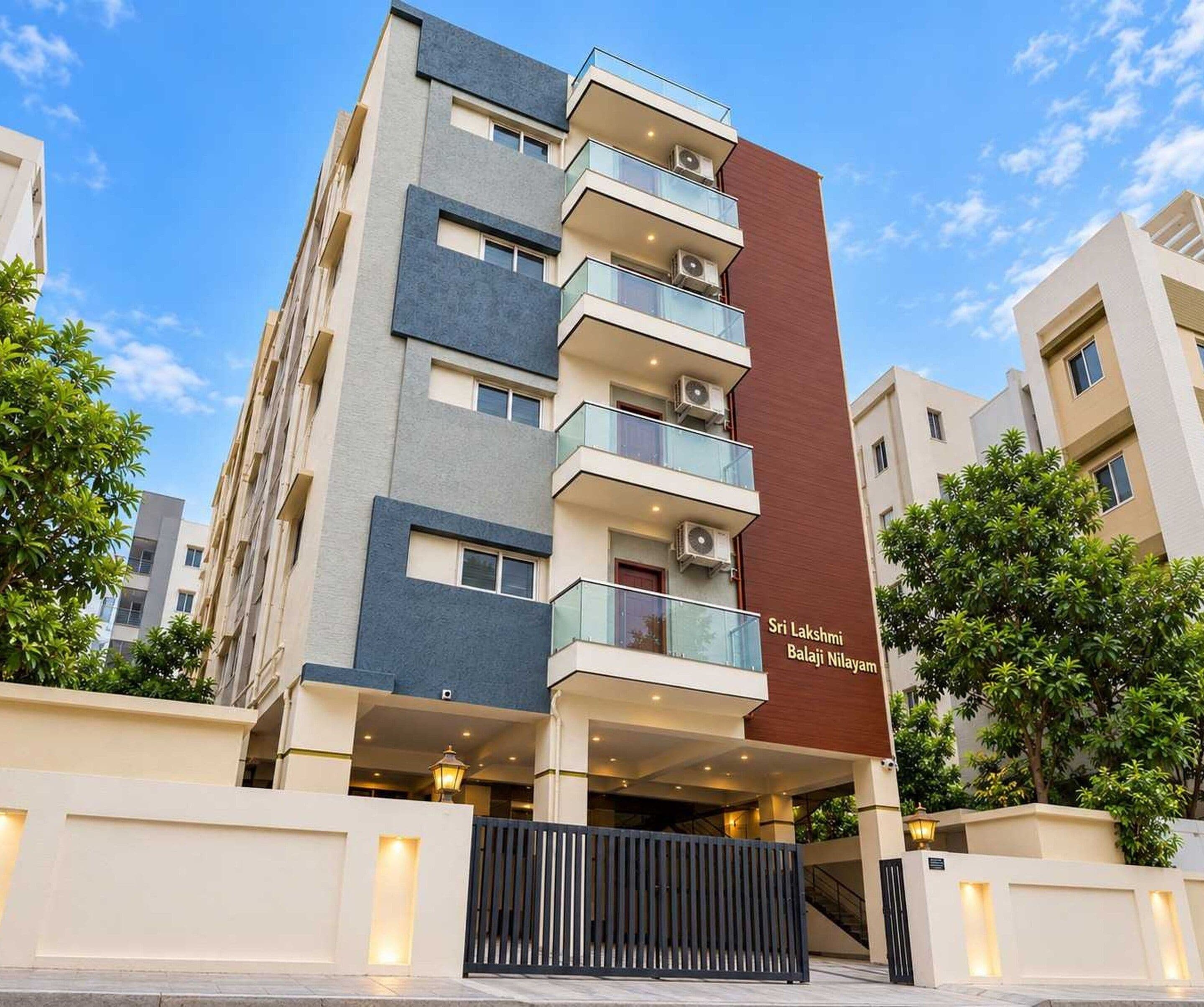 A multi-story residential building with balconies, a gated entrance, and a clear sky.