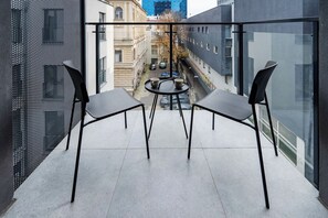 Ein Balkon mit zwei Stühlen und einem kleinen Tisch, mit Blick auf eine Stadtstraße.