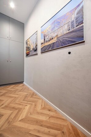 Een gang met een houten visgraten vloer, een grijze garderobe en twee ingelijste foto's aan de muur.