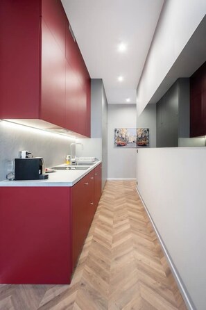 Een moderne keuken met een visgraat houten vloer, rode keukenkastjes en een centraal kookeiland met een spoelbak en aanrecht.