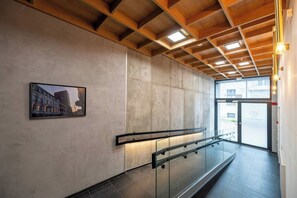 A modern interior with a concrete wall, a glass railing, and a framed picture. - Łódź Roosevelta Studio A — Balcony & A/C (Łódź)