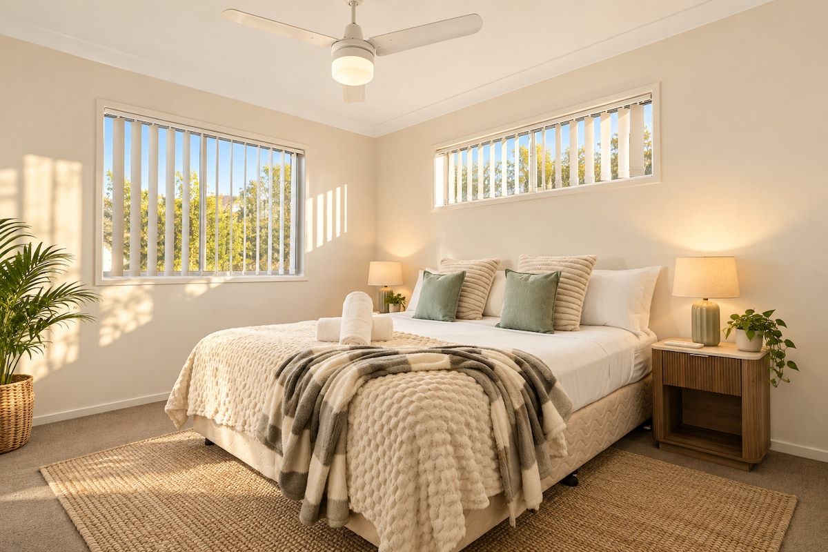 A bedroom with a bed, two bedside tables, a ceiling fan, and large windows.
