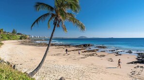 A beach with a palm tree, rocky shoreline, and people walking. - Coastal-Style 3BR Townhouse - Mountain Creek (Mountain Creek)
